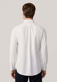 Camisa blanca de manga larga con cuello clásico, tapeta de botones y dobladillo redondeado. Presenta una textura sutil y puños abotonados.