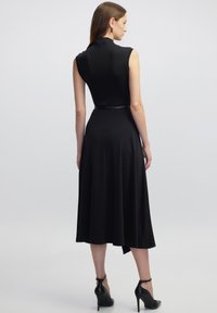 Schwarzes ärmelloses Kleid mit einem taillierten Oberteil und einem ausgestellten Rock, aus glattem Stoff gefertigt, mit einem taillierten Bund und Sandalen mit Knöchelriemen.