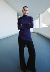 Haut bleu marine à col montant et manches longues, associé à un pantalon noir à jambes larges avec des accents en dentelle le long de l'ourlet, sur un fond minimaliste.