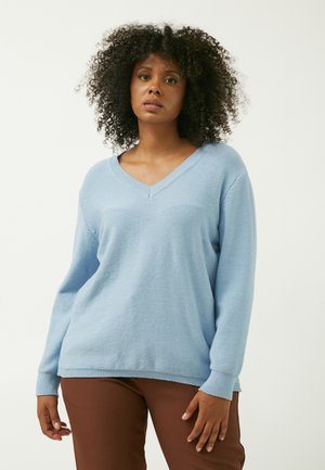 Pull en tricot bleu clair avec un col en V et des manches longues, doté d'un tissu texturé et de poignets côtelés, assorti à un pantalon marron.