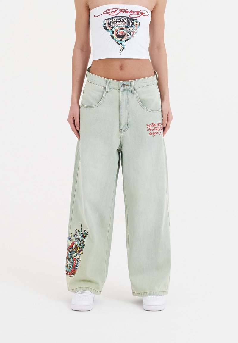 Lichtgroene wijde jeans met geborduurde drakenmotieven in meerdere kleuren.Heeft standaardzakken en zichtbare stiksels. Gecombineerd met een witte top.