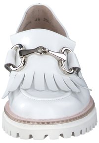 Witte lakleren schoen met franjes, zilveren hardware-accent, dikke witte zool, ronde neus en een gladde textuur.