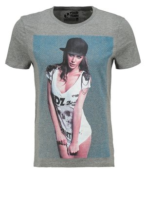 Kobieta nosząca czarną czapkę i białą sukienkę z nadrukiem graficznym na szarym t-shircie z logo "Your Turn" na linii szyi.