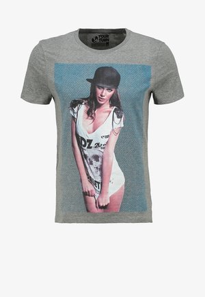 Kobieta nosząca czarną czapkę i białą sukienkę z nadrukiem graficznym na szarym t-shircie z logo "Your Turn" na linii szyi.