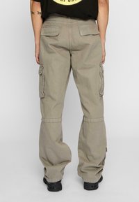 Pantalon cargo beige à la coupe décontractée, doté de plusieurs poches latérales, d'un poignet ourlé et d'un tissu texturé. Vue arrière affichée.