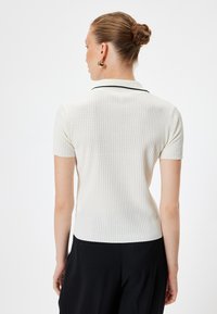Polo shirt a maniche corte in tessuto bianco texturizzato con un motivo a coste e piping nero lungo il colletto. Presenta una silhouette aderente.