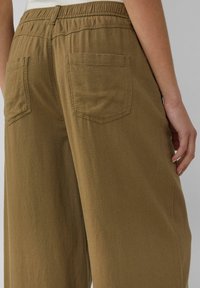 Pantaloni a gamba larga verde oliva con elastico in vita, dotati di due tasche posteriori e in un tessuto morbido e strutturato.