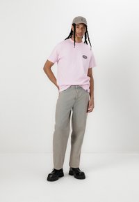 Camiseta de algodón rosa con logo, jeans de mezclilla gris claro y zapatos de plataforma negros. Además, una gorra gris con un logo.