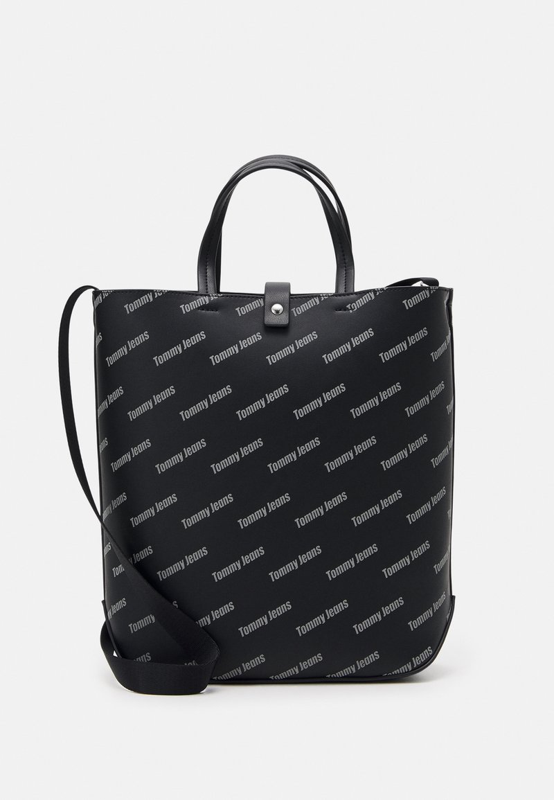 Sac fourre-tout rectangulaire noir avec deux poignées supérieures, bandoulière ajustable, fermeture à pression, et motif logo "Tommy Jeans" sur toute la surface.