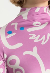 Im Schnitt tailliertes Langarmoberteil aus pinkfarbenem Stoff mit weißen abstrakten Mustern und blauen Punkten, mit einer glatten Textur und hohem Ausschnitt.