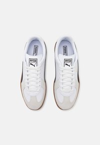 Baskets blanches et grises avec une tige en daim et synthétique, dotées d'accents noirs, d'une semelle en caoutchouc et de lacets plats. Logo Puma sur la languette.