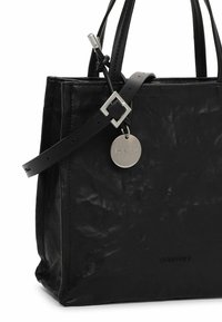 Sac cabas en cuir noir avec poignées doubles, sangle ajustable, boucle argentée et étiquette métallique ronde embossée du nom de la marque.