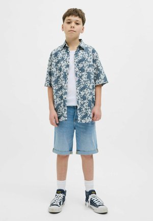Chemise florale bleue à manches courtes sur un T-shirt blanc, associée à un short en denim bleu clair et des baskets navy avec des accents blancs.