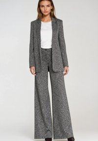 Marynarka w kratę i luźne spodnie o szerokich nogawkach w czarno-białe wzory, zestawione z prostą białą bluzką. Tkanina wygląda na fakturowaną.