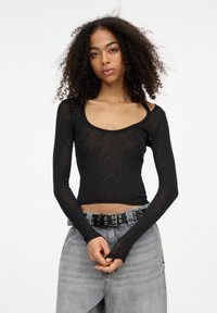 Maglietta nera a maniche lunghe con scollo rotondo, realizzata in tessuto trasparente. Abbinata a jeans in denim grigio chiaro a vita alta e una cintura nera.