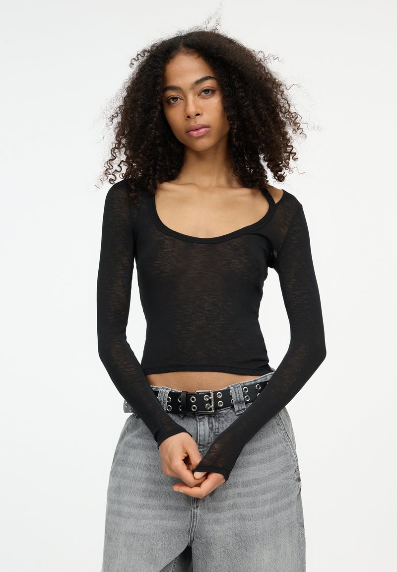 Maglietta nera a maniche lunghe con scollo rotondo, realizzata in tessuto trasparente. Abbinata a jeans in denim grigio chiaro a vita alta e una cintura nera.