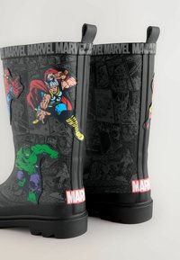 Mustat kumiset sateenkenkä, joissa on Marvel-superheroita kirkkaissa väreissä. Kenkien pinnassa on kuvia Hulkista, Spidermanistä ja Thorista, taustalla on sarjakuvamainen kuvio.