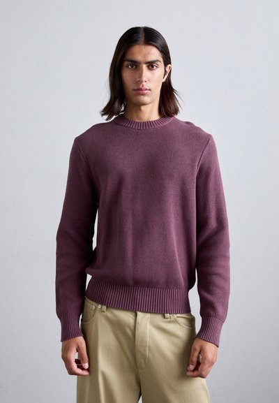 Maglione a collo rotondo lavorato a maglia in un profondo bordeaux. Morbida consistenza, polsini e orlo a coste, abbinato a pantaloni beige chiaro, che mostrano una vestibilità rilassata.
