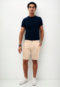 Marineblaues T-Shirt, slim fit, kombiniert mit hellbeigen Shorts mit Knopfverschluss. Weiße Sneakers vervollständigen das Outfit. Einfaches, lässiges Design.