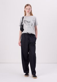 T-shirt en coton gris avec un imprimé papillon, associée à un pantalon noir ample et à des baskets noires. Complétée par un petit sac bandoulière noir.
