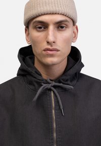 Black hooded jacket with a zipper front and grey drawstring. The fabric has a smooth texture, featuring a simple design without patterns.
