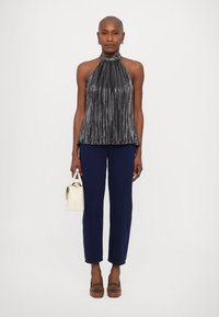 Melnā pludlīniju halter top, pieguļošs, saskaņots ar tumši ziliem biksēm; modele tur mazu baltu somu un valkā brūnus platformas sandales.