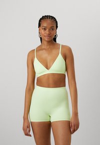 Soutien-gorge de sport côtelé vert clair en forme triangulaire avec des bretelles réglables, associé à un short taille haute assorti. Les deux présentent un petit logo.
