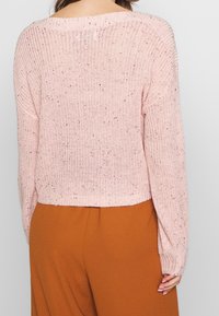 Jasnoróżowy dziergany sweter o luźnym kroju, z żebrowanym wykończeniem i skropionymi detalami, z szerokim dekoltem i krótkim dołem.