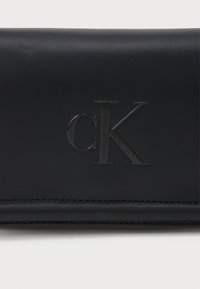 Portafogli in pelle nera con logo "CK" impresso, texture liscia, linee pulite e dettagli di cucitura a contrasto lungo i bordi.