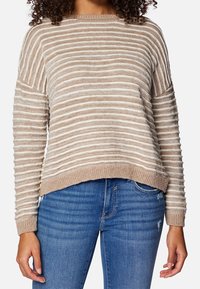 Beżowy sweter dziany w poziome białe paski, z okrągłym dekoltem i prążkowanymi mankietami. Połączony z niebieskimi dżinsami.