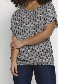 Haut à motif en noir et blanc avec un motif d'éventail, manches courtes et coupe ample, associé à un jean bleu foncé. Texture de tissu douce.