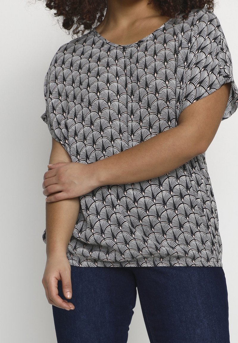 Haut à motif en noir et blanc avec un motif d'éventail, manches courtes et coupe ample, associé à un jean bleu foncé. Texture de tissu douce.