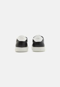 Sneaker in pelle nera con dettagli bianchi sul tallone, dotati di punta tonda e suola in gomma testurizzata. Il marchio è visibile sul tallone.