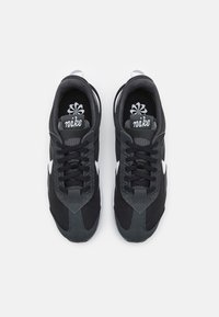 Black athletic shoes featuring mesh and synthetic materials, with a white logo, flat laces, and a textured grey toe cap.