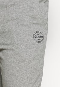 Pantalones de chándal de algodón grises con una superficie texturizada y un parche circular de logo que incluye el texto "Jack & Jones" y "Originals".