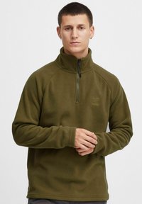 Ciemnozielony polarowy sweter z wysokim kołnierzem, zamek błyskawiczny z przodu do połowy oraz lekką teksturą, z rękawami raglanowymi i detalem logo na piersi.