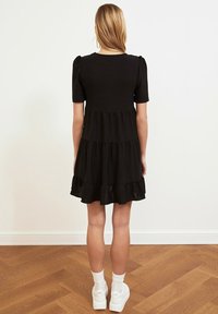 Robe noire à volants avec de courtes manches bouffantes, présentant un ourlet à volants et une texture lisse. Portée avec des baskets blanches et des chaussettes à la cheville.