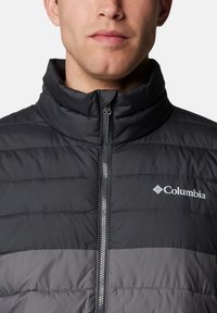 Schwarze und graue gepolsterte Jacke mit hohem Kragen, durchgehendem Reißverschluss und Columbia-Logo auf der linken oberen Seite. Strukturierter Stoff mit horizontalen Nähten.