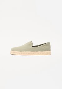 Chaussure slip-on en toile verte avec un bout arrondi et une semelle en jute tressé. Présente des coutures minimales et une coupe à la cheville pour une meilleure respirabilité.
