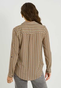 Blusa de manga larga con un patrón geométrico que presenta diamantes en amarillo, naranja y azul marino, con cuello puntiagudo y puños abotonados.