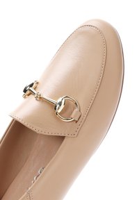 Beige leren instapper met een ronde neus, goudkleurige hardware-accent en gestikte details langs de randen. Soepele textuur.