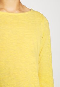 Gelbes Langarmshirt mit Rundhalsausschnitt, leichtem Stoff und einem dezenten strukturierten Muster. Keine sichtbaren Logos oder Verzierungen.