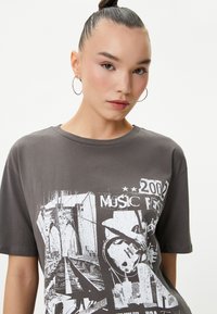 Grå bomulds t-shirt med korte ærmer og rund halsudskæring, med et hvidt grafisk print af en bro, guitar og "2002 MUSIC FEST."