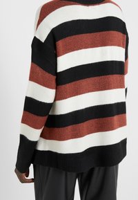 Pruhovaný pletený svetr s širokými pruhy v černé, bílé a měděné barvě. Design zahrnuje uvolněný střih a žebrované manžety a lem.