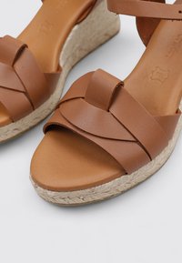 Sandalias de cuña marrones con correas de cuero cruzadas, un upper de acabado suave y un talón de cuña envuelto en yute. Un diseño casual y texturizado.