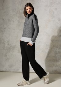 Pull en tricot gris et noir avec un col montant et un ourlet rayé, associé à un pantalon noir et des baskets légères. Texture lisse et coupe décontractée.