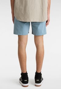 Lysblå shorts med en glat tekstur, som har en lige pasform. Båret med sorte sokker og Vans fodtøj. Stribet skjorte delvist synlig.