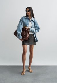Denim jacket with a light blue hue, fitted white ribbed top, brown leather handbag, grey mini skirt, and yellow strappy sandals.
