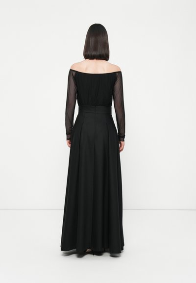 Zwarte off-the-shoulder lange jurk met lange doorzichtige mouwen. Strakke lijfje met een geplooide rok en ritssluiting aan de achterkant. Volledige lengte.