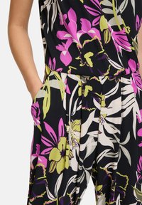 Blommig jumpsuit i svart med rosa, gröna och vita blommor. Har vida ben, sidofickor och en lös passform för komfort. Mjuk tygtextur.